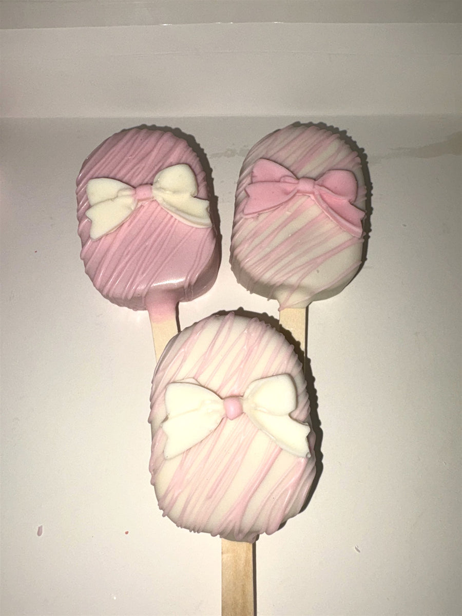 Assorted pink-dipped cakesicles with bows on sticks